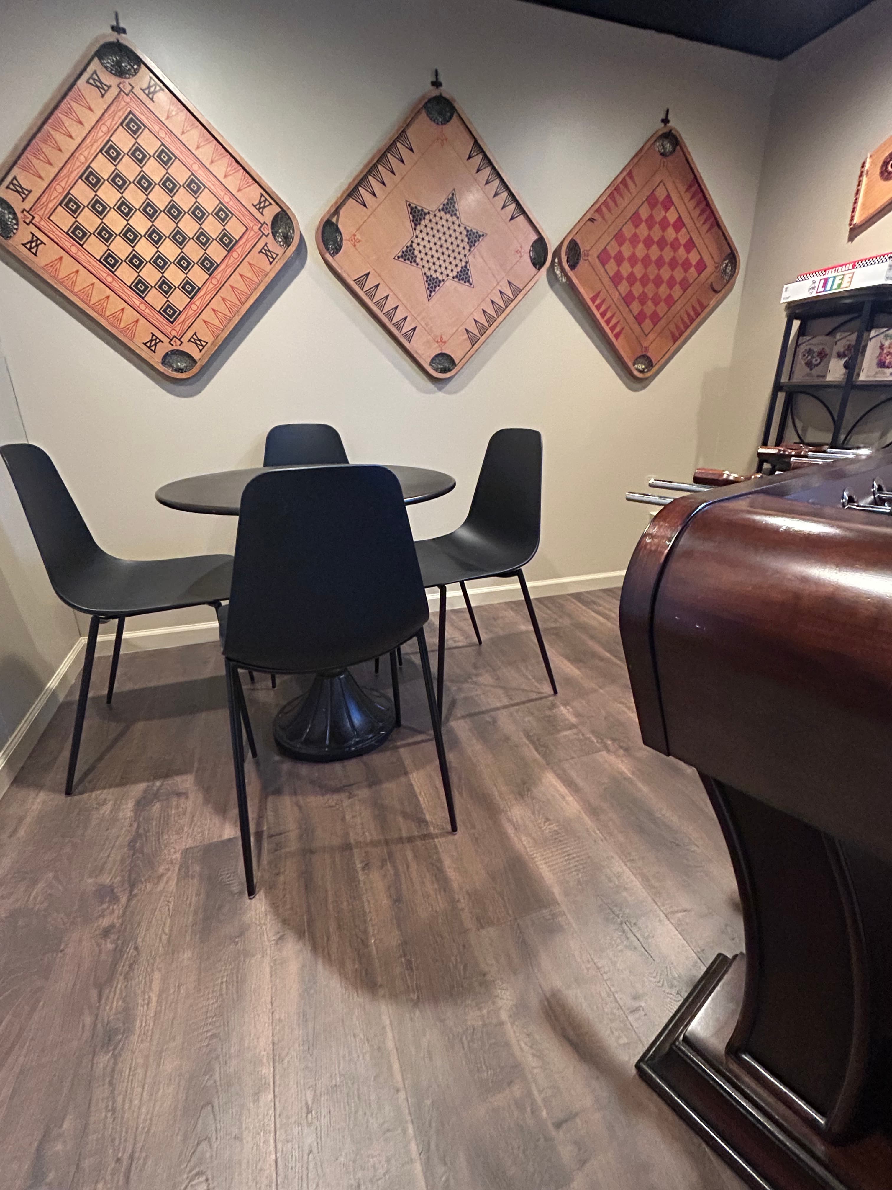 Room with brown floor, black table and chairs and game boards hung on the wall.