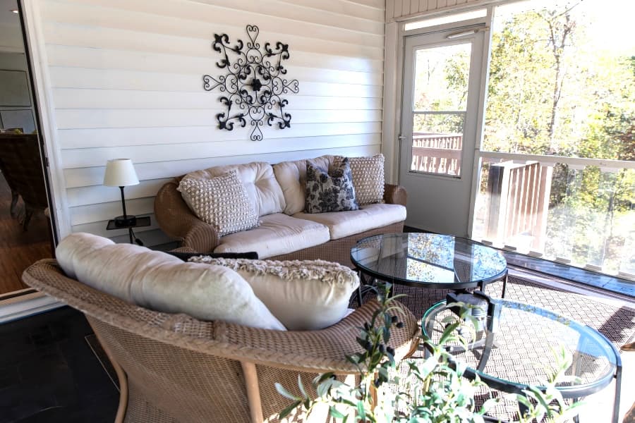 Covered and screened porch overlooking the river with sofa, chair and tables
