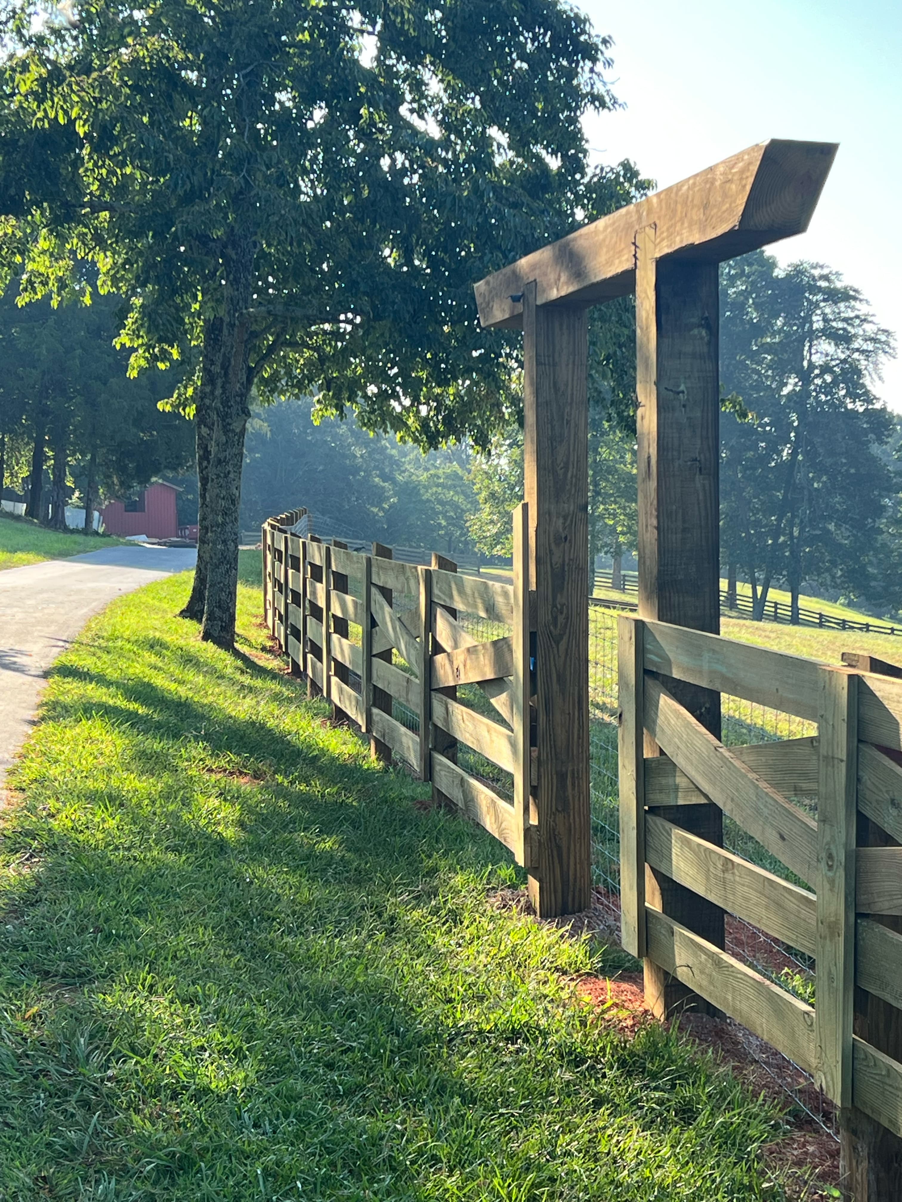 A wooden fence and gate line a grassy path under sunlight.