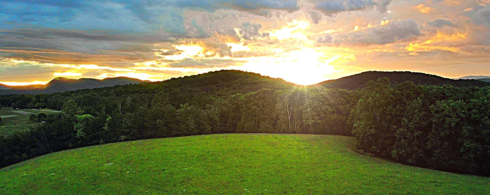 A vibrant sunset casts golden light over rolling green hills.