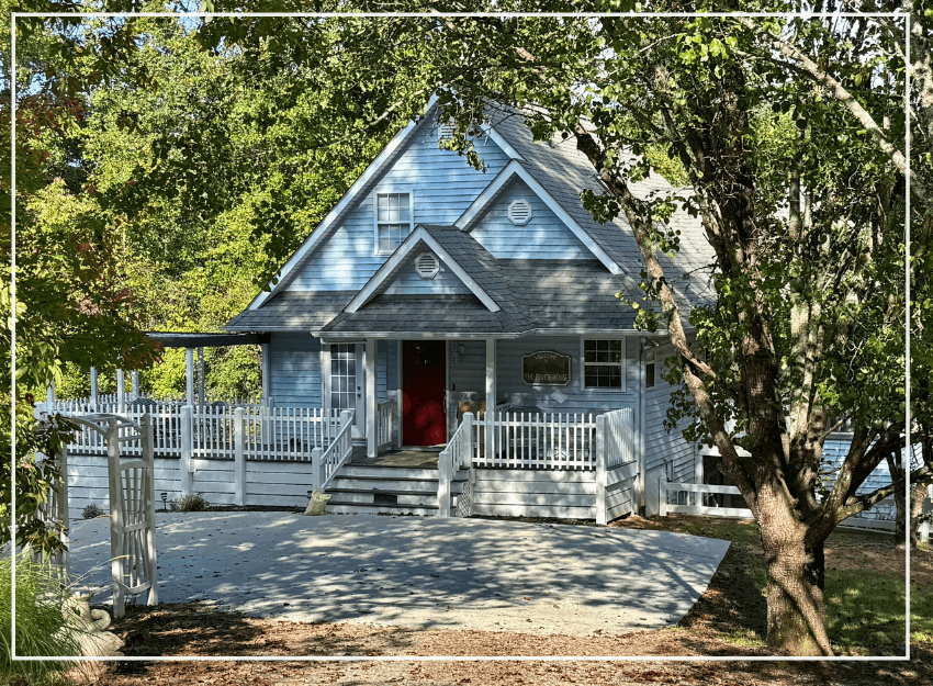 A blue house with a red door surrounded by trees and a white railing.